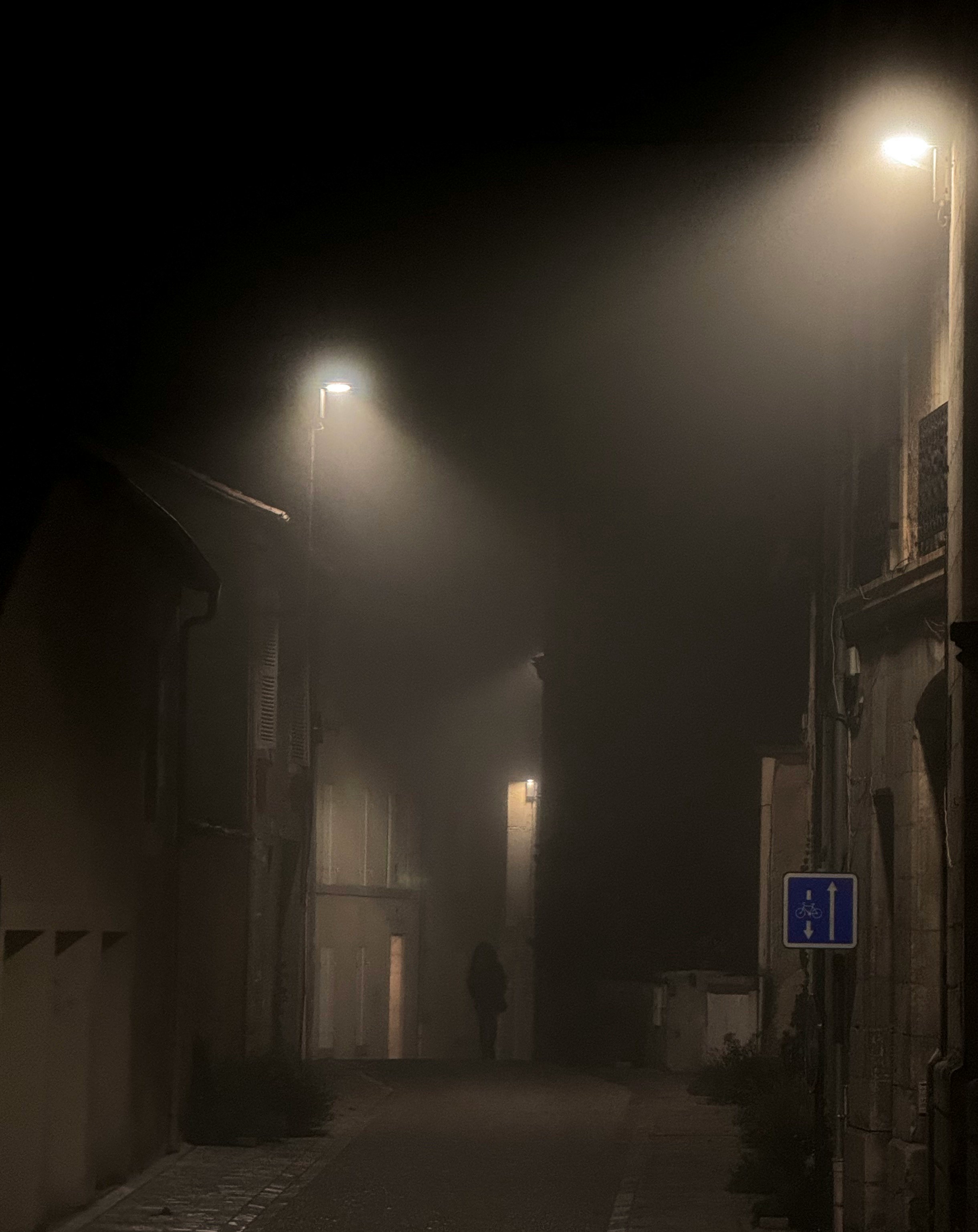 Photo of a person walking in a dark foggy alley under street lamps